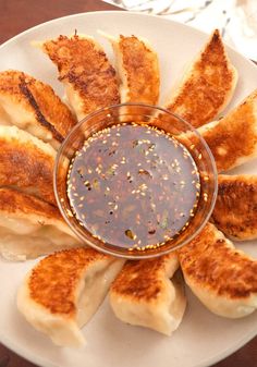 a white plate topped with dumplings covered in sauce on top of a wooden table