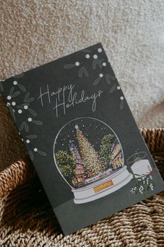 a happy holidays card with a snow globe in the center and trees inside it on top of a wicker basket