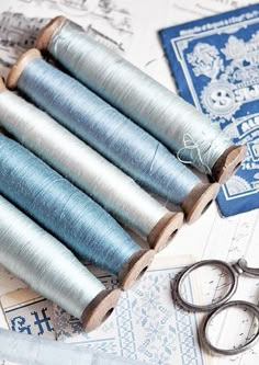 several spools of thread sitting next to scissors on top of blue and white papers