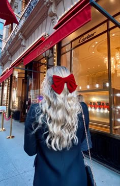 a woman with long blonde hair wearing a red bow in front of a storefront