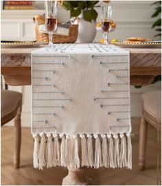 a white table runner with tassels and beads on it, sitting at a dining room table