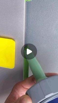 a hand holding a green marker near a yellow and gray button on a white wall