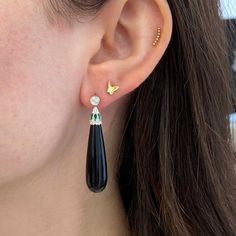 A gorgeous pair of dangling earrings inspired by the Art Deco Era. The tops feature two bezel-set old European cut diamonds with a total combined weight of approximately 0.53 carats. Set below are alternating green enamel and additional old European cut diamonds set in a heart motif. The total weight of these additional diamonds is approximately 0.27 carats. Two pieces of polished onyx are set below the diamonds. These earrings are handcrafted in platinum.
The length of these earrings measures 1 Elegant Onyx Drop Jewelry, Elegant Black Enamel Drop Earrings, Elegant Black Enamel Dangle Jewelry, Elegant Drop Jewelry With Bezel Setting, Elegant Teardrop Bezel Set Earrings, Elegant Black Enamel Earrings For Anniversary, Classic Single Diamond Earring For Evening, Luxury Bezel Set Drop Earrings, Luxury Bezel-set Drop Earrings