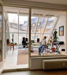 two people are sitting in an open room with large windows and plants on the floor