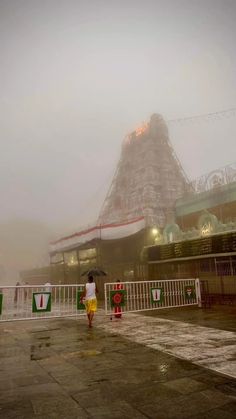 a person with an umbrella is walking in the rain near a roller coaster at night