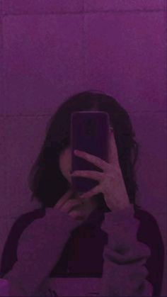 a woman taking a selfie in front of a purple wall with her cell phone