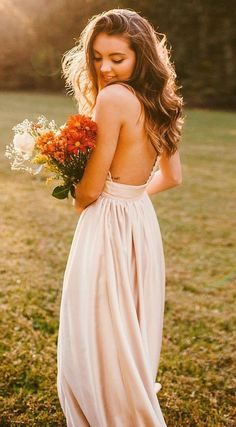 a woman in a long dress holding flowers and looking down at her back with the sun shining on her