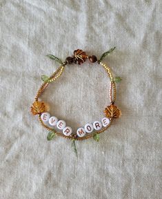 a beaded bracelet with the word love on it and flowers in beads is laying on a white cloth