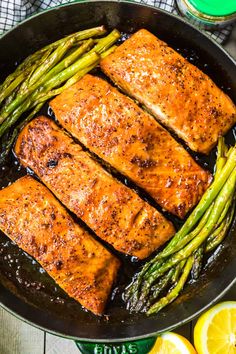 salmon and asparagus cooking in a skillet with lemons on the side