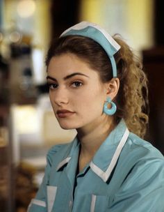 a woman in scrubs is looking at the camera and has big earrings on her head