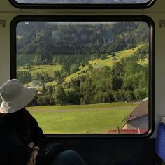 a woman sitting on top of a train looking out the window at a green field