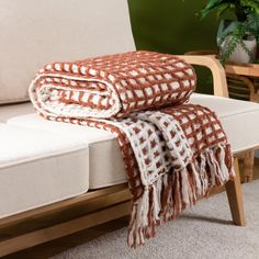 two blankets folded on top of a couch in front of a chair and potted plant