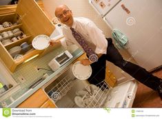 a man is holding plates in his kitchen while he stands on the dishwasher