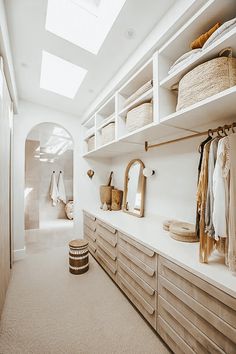 a walk in closet filled with lots of clothes and baskets on top of wooden shelves