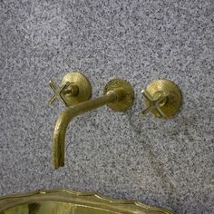 two brass faucets on the wall next to a mirror