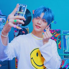 a young man with blue hair holding up a cell phone in front of his face