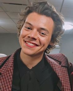 a young man with curly hair smiling at the camera while wearing a suit and tie