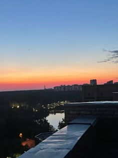 the sun is setting over some water and buildings with lights on in the distance as seen from a rooftop