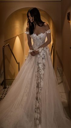 a woman in a wedding dress is standing on the stairs with her hands behind her back