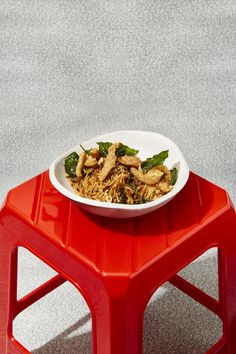 a bowl of food sitting on top of a red plastic stool next to a white plate