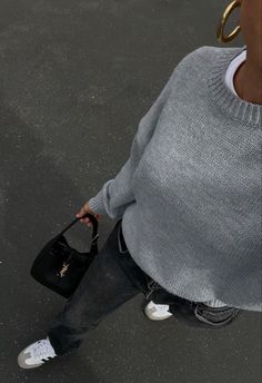 an overhead view of a woman carrying a black purse and wearing a gray sweater with gold hoop earrings