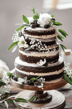 a three tiered cake with flowers and greenery on top is sitting on a wooden table