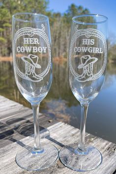 two wine glasses sitting on top of a wooden table next to a body of water