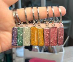 a person holding five different colored glittered items in their hand, each with a keychain