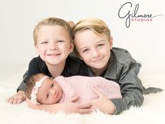 two young children laying next to each other on a white blanket with their arms around the baby's head