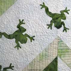 two green lizards sitting on top of a quilt