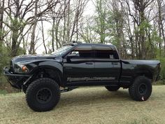 a large black truck parked on top of a grass covered field in front of trees