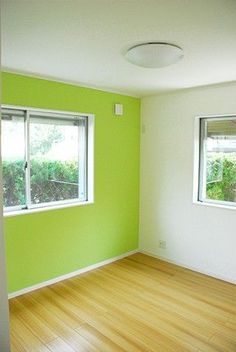 an empty room with green walls and wooden floors, two windows on the far wall