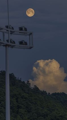 the full moon is setting over some hills and clouds in the sky, with people sitting on a bench at the top