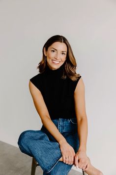 a woman sitting on a chair with her legs crossed and smiling at the camera,