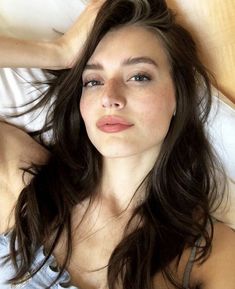 a woman laying on top of a bed next to a wooden head board with her hair blowing in the wind