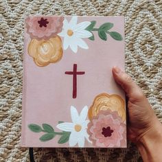 a hand holding up a pink paper with flowers on it and a cross painted on the front