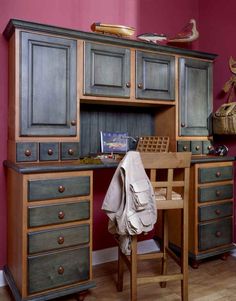 an old fashioned wooden desk and chair in a room with red walls, wood floors and cabinets