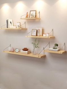 three wooden shelves on the wall with pictures, books and other items in vases