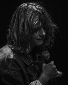 a woman with long hair holding a microphone in front of her face and wearing a denim jacket