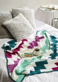 a blanket on top of a bed next to two pillows and a tray with food