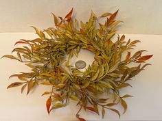 a wreath made out of dried leaves on a white counter top with a coin in the center