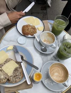 a table topped with plates of food next to cups of coffee and juices on top of it