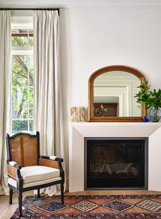 a living room with a fireplace, mirror and chair