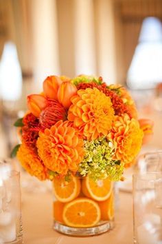 an arrangement of oranges, carnations and other flowers in a glass vase