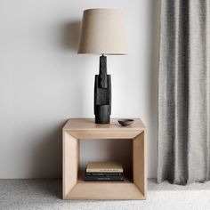 a nightstand with a lamp on it next to a curtained window in a white room