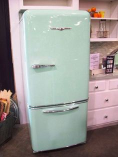 a mint green refrigerator in a kitchen next to white cupboards and shelves with utensils