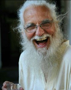 an old man with white hair and glasses holding a glass in one hand and laughing