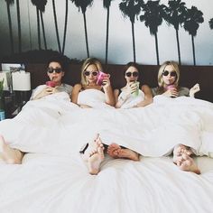 three women laying in bed with their feet up on the pillows while one woman is holding a cell phone