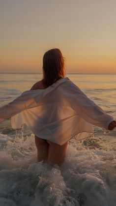 a woman standing in the ocean at sunset