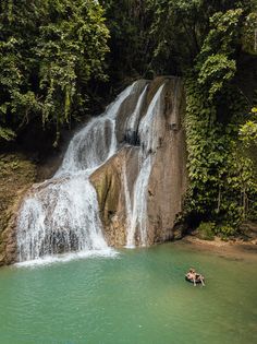 two people are floating in a raft near a waterfall with a man standing on it